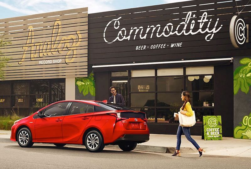 A man is putting groceries in the back of his prius while a woman approaches