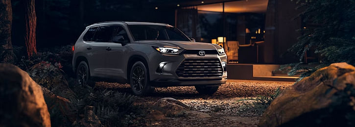 A grey Toyota Grand Highlander parked in the forest next to the cozy house
