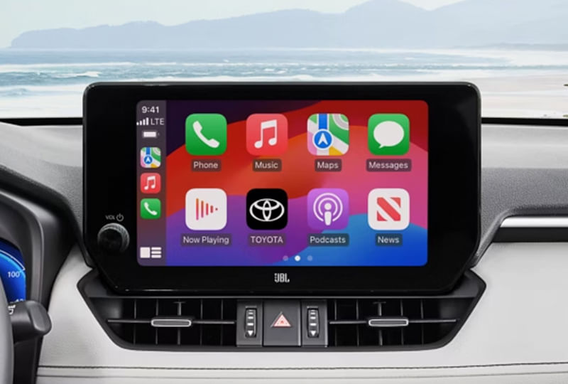 Close-up of a Toyota RAV4's infotainment screen displaying Apple CarPlay interface with icons for Phone, Music, Maps, and Toyota, with JBL branding below.