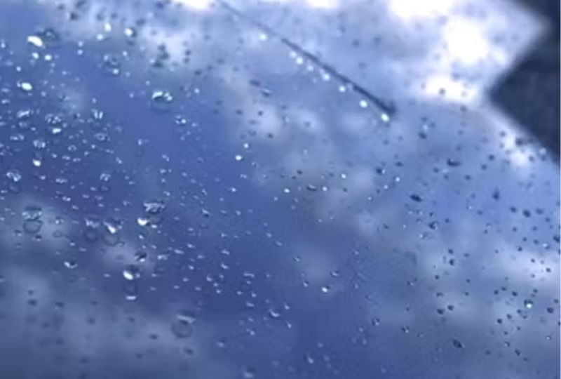 Raindrops streak down a car window, creating a blurred view of the outside scenery.