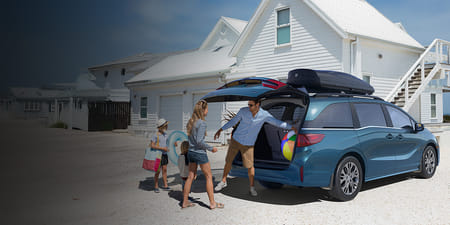 A blue 2026 Odyssey parked by a beach house as a family unloads beach items from the trunk.