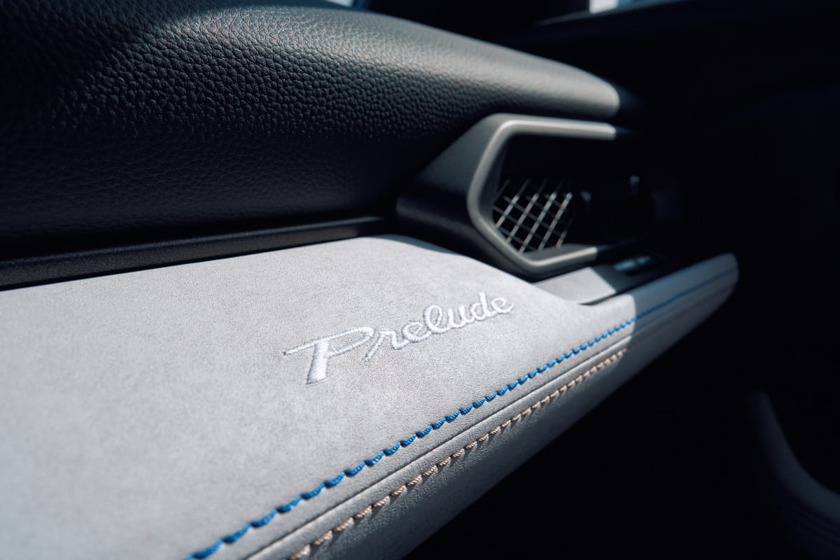 A detailed shot of the passenger-side dashboard of the 2026 Honda Prelude, showing the Prelude name embroidered in script on a soft, light-colored material with blue accent stitching.