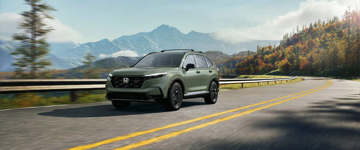 A green Honda CR-V driving along a winding road with mountains in the background.