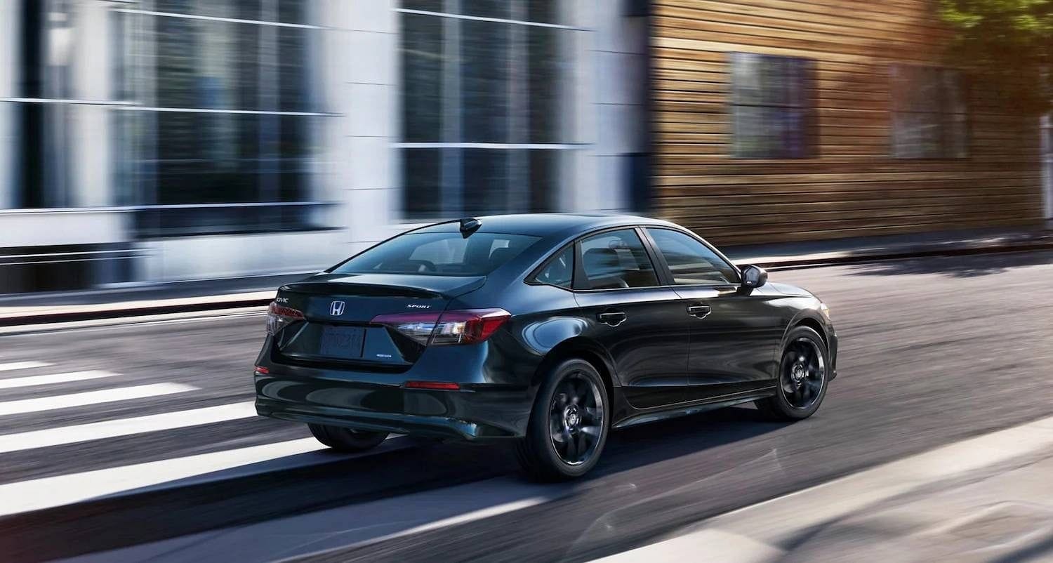 The 2025 Honda Civic Sedan Sport Hybrid in Crystal Black Pearl at 7/8 rear passenger side angle in urban street corner outdoor environment
