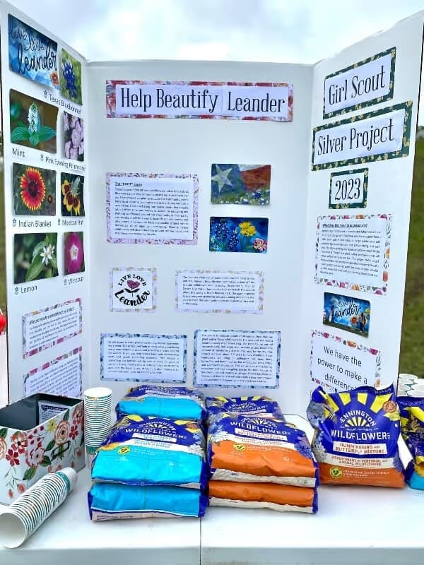 Tri-fold poster display titled "Help Beautify Leander" for a Girl Scout Silver Project 2023. Features wildflower seed bags and illustrated plant guides. Bright, informative, and community-focused.