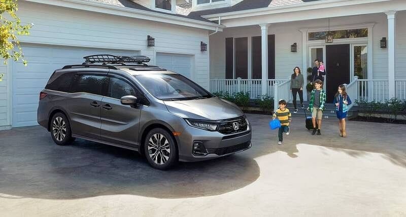 The 2026 Honda Odyssey Elite in Modern Steel Metallic with accessories parked in front of a house with family walking to the vehicle