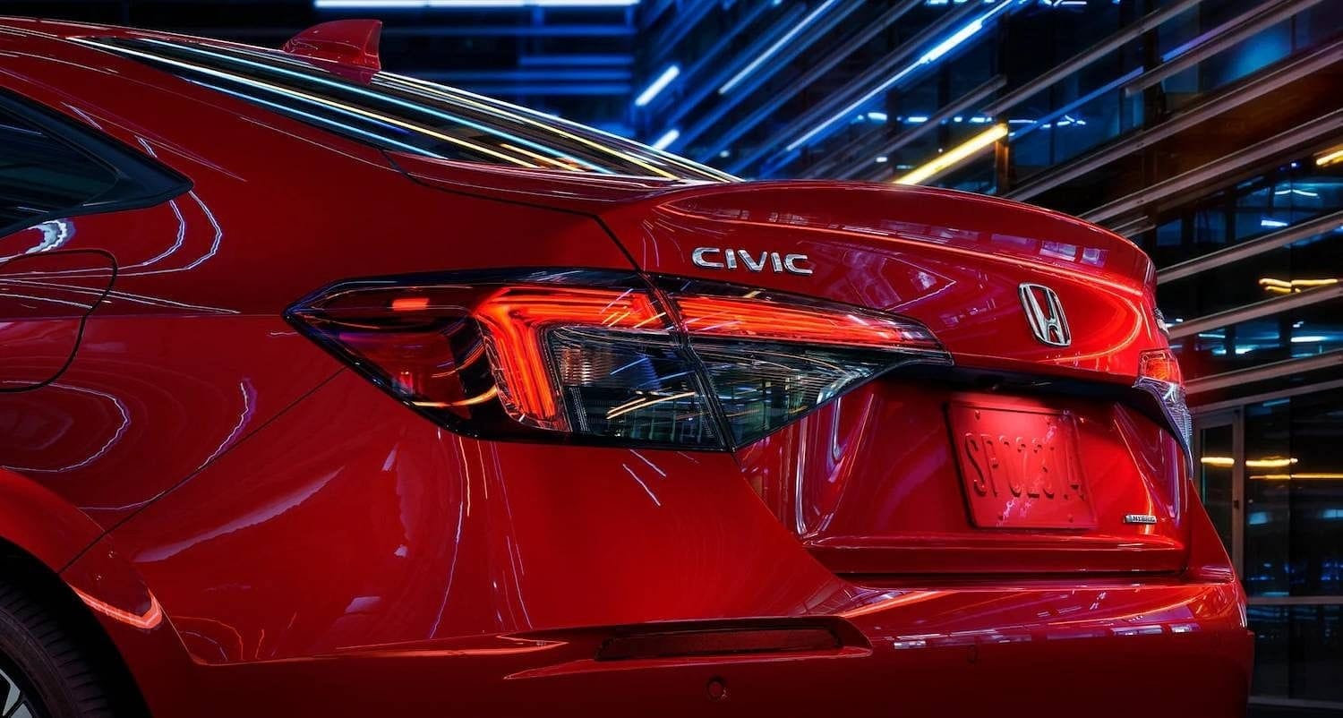 The 2025 Honda Civic Sedan Sport Touring Hybrid in Rallye Red at 3/4 driver rear angle in outdoor environment