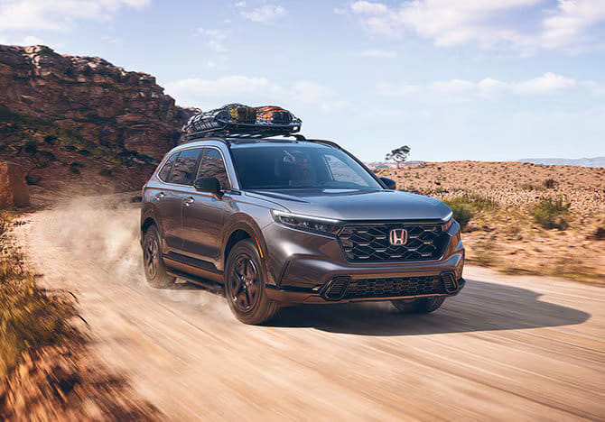 Grey used Honda CR-V driving on a dirt road with roof rack