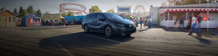 The 2026 Honda Odyssey Elite shown in Smoke Blue Pearl on a wooden pier of an amusement park