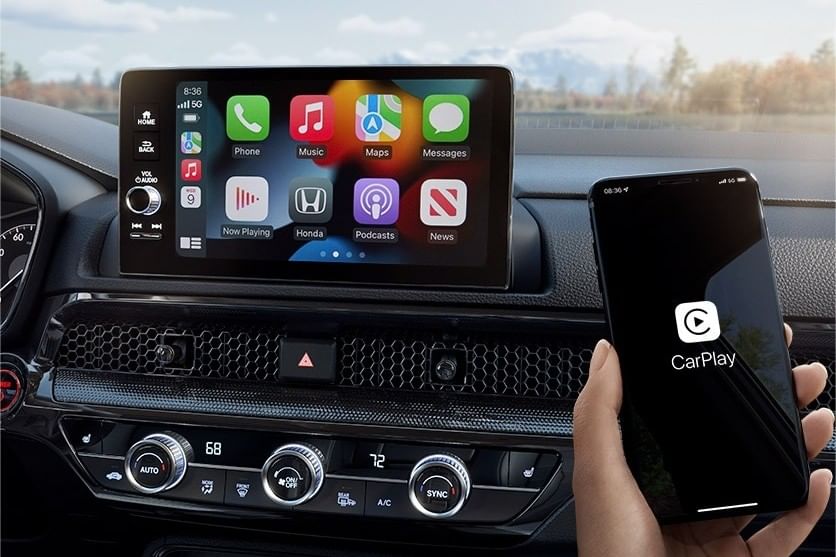A used Honda CR-V Hybrid interior featuring a digital display with Apple CarPlay apps and a hand holding a smartphone displaying the CarPlay logo.