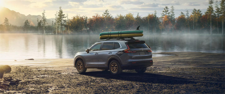 Gray used Honda CR-V with HPD package and boards on roof rack parked by a lake.