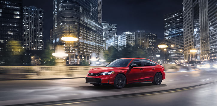 A red Civic driving through a city at night.