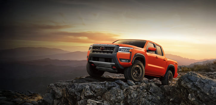 A red 2026 Frontier PRO-4X on a rocky outcrop in the mountains with the sunset behind.