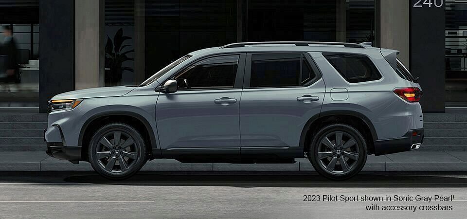 2023 Honda Pilot Sport shown in Sonic Gray Pearl with accessory crossbars standing by the building