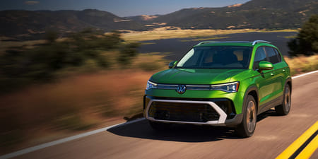 A green 2026 Taos driving with a small lake and mountains in the background.