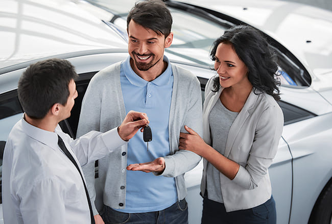 Salesperson handing car keys to a smiling couple at a dealership