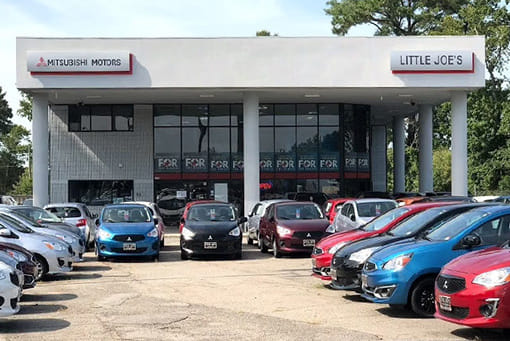 A car dealership with a variety of vehicles parked in front, featuring Mitsubishi Motors signage. The tone is inviting and professional.