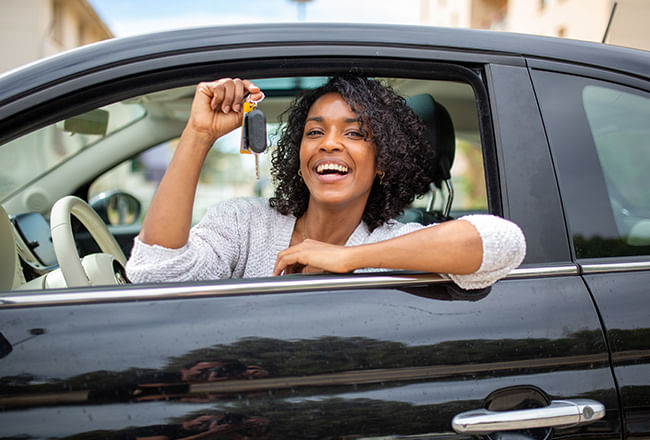 A person sitting in a car holds up car keys, smiling.
