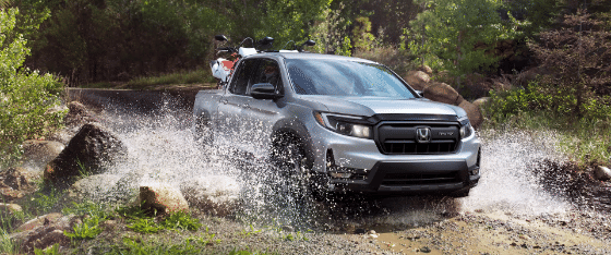 2026 Honda Ridgeline Sport in Solar Silver Metallic driving through water with dirt bikes in back.