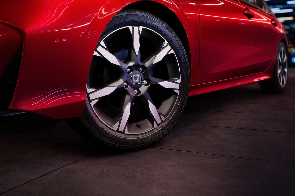 Close-up of a red 2026 Honda Civic Sedan front wheel on a dark, reflective floor. The alloy wheel features a bold design, creating a sleek and dynamic appearance.