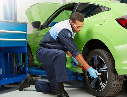 Service technician tightening the rear wheel on a green honda