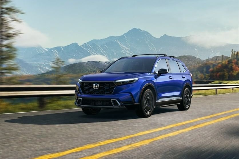 Un Honda CR-V Hybrid 2025 circula por una carretera sinuosa con un fondo de montañas y cielos despejados, mostrando un diseño elegante y moderno.