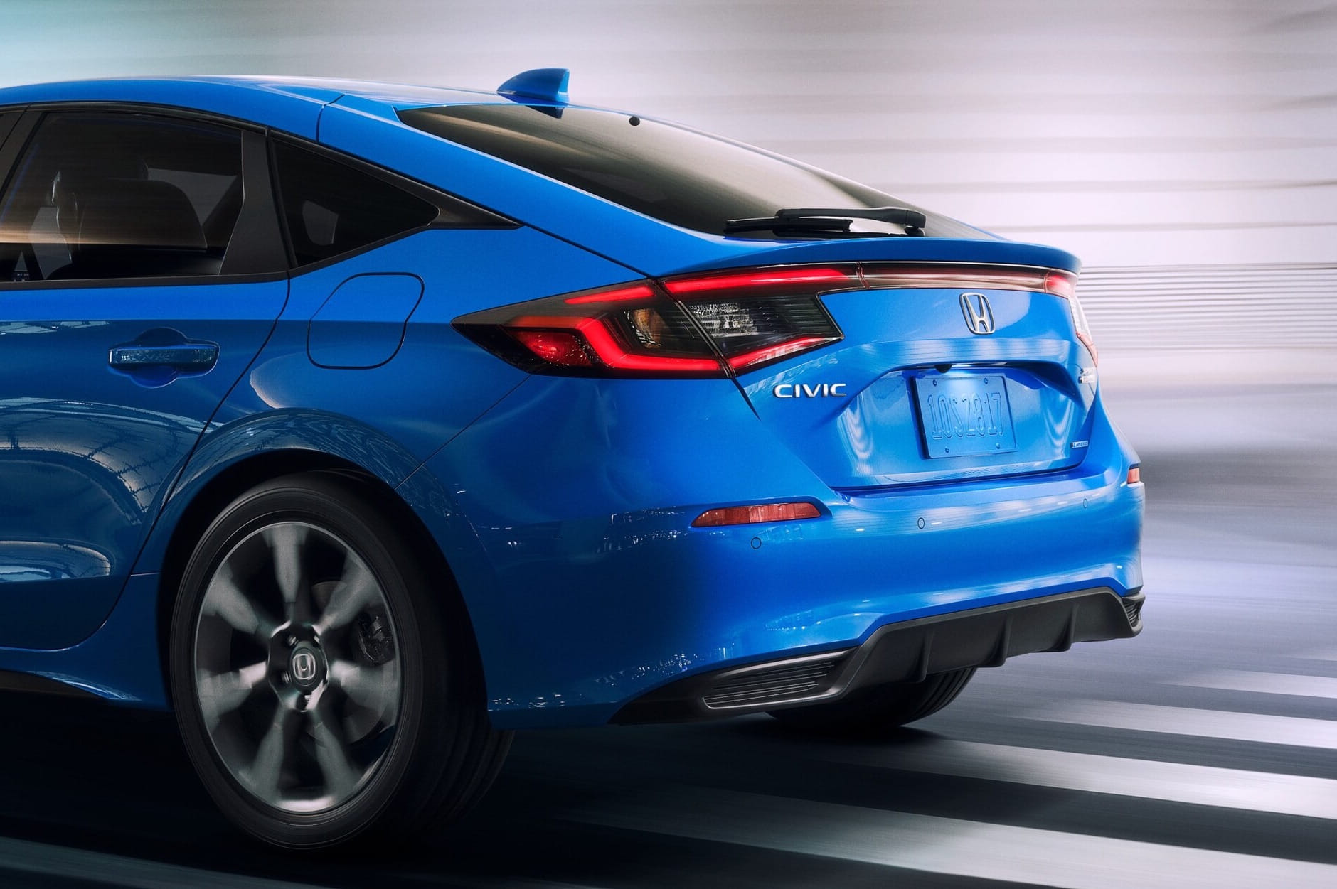 Un vibrante Honda Civic Hatchback 2026 azul se captura desde un ángulo trasero, mostrando líneas elegantes y luces traseras modernas. El coche está en movimiento, transmitiendo velocidad y estilo.