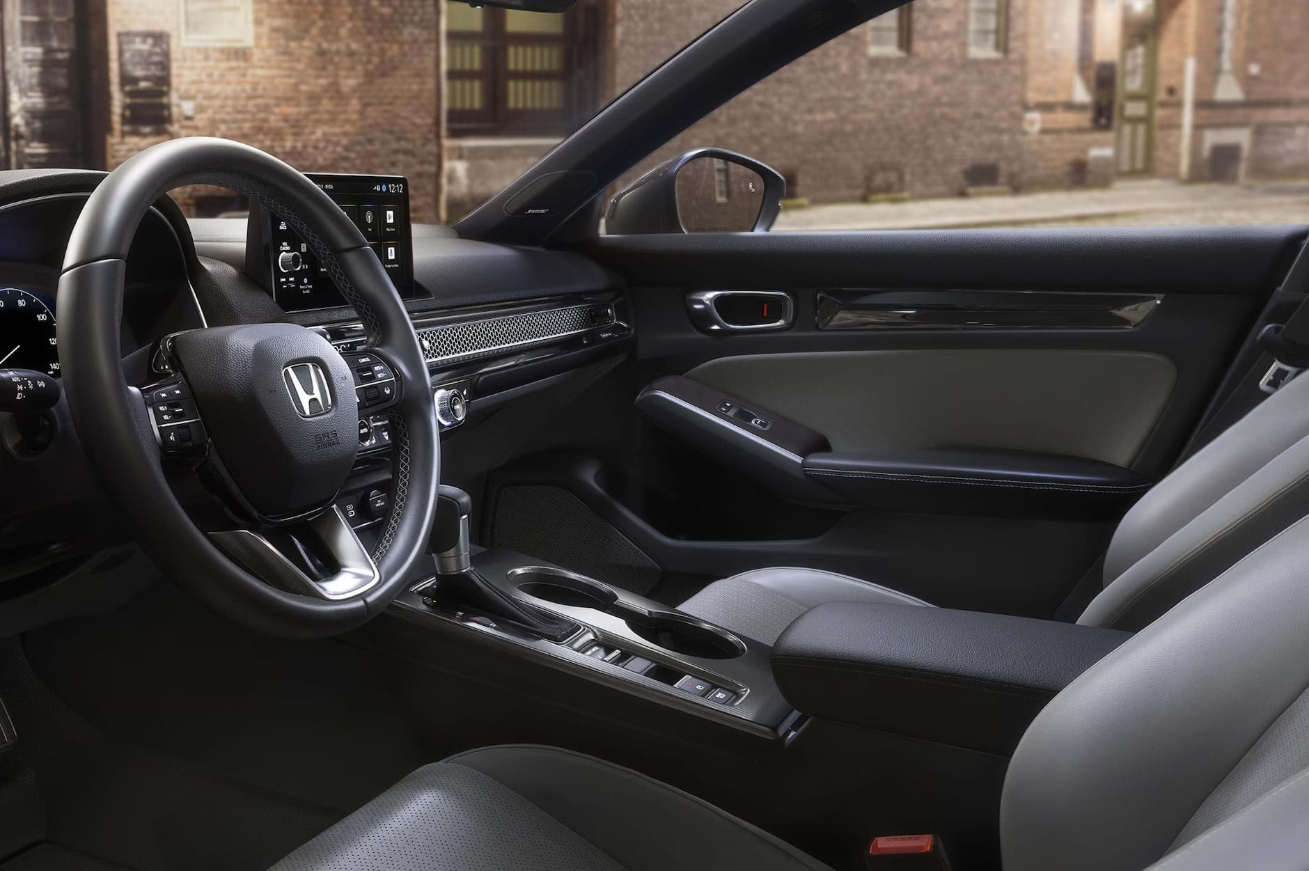 Interior del Honda Civic Hatchback 2026 con un volante negro con el logotipo de Honda, salpicadero elegante, pantalla digital y asientos de cuero, con un fondo urbano desenfocado.