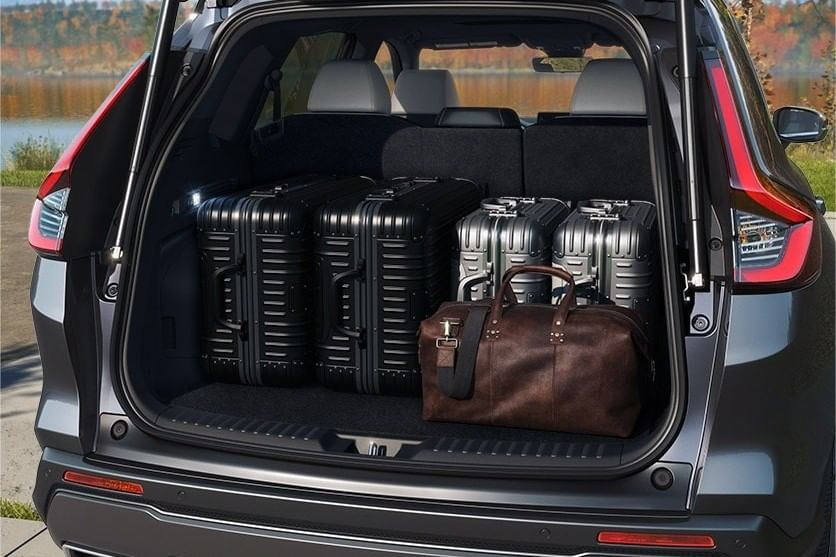 El maletero de un Honda CR-V Hybrid 2025 lleno con cuatro maletas rígidas negras y un bolso de cuero marrón, con un fondo escénico.