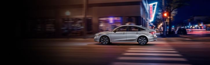2025 Honda Civic Sedan Sport Touring Hybrid in Solar Silver Metallic driving on urban street at night