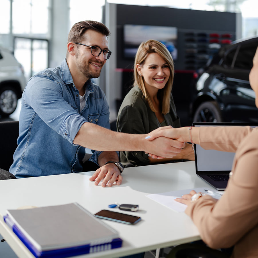 Couple shaking hands with salesperson at dealership