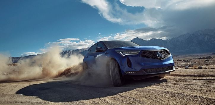 A blue RDX driving in the desert kicking up clouds of dust.