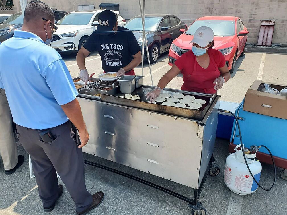 People serving tacos from a food cart