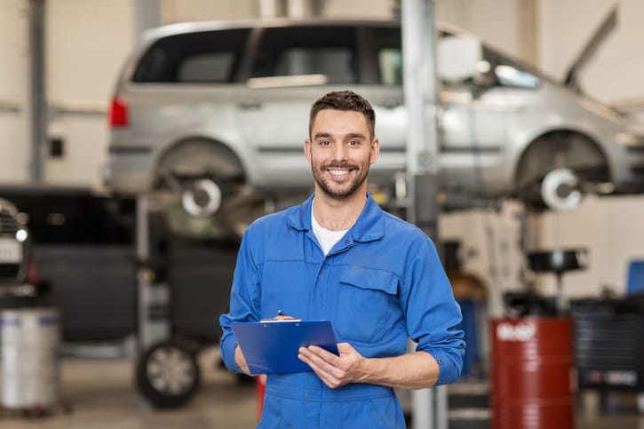 Happy technician in car repair shop in front of a car on a lift.
