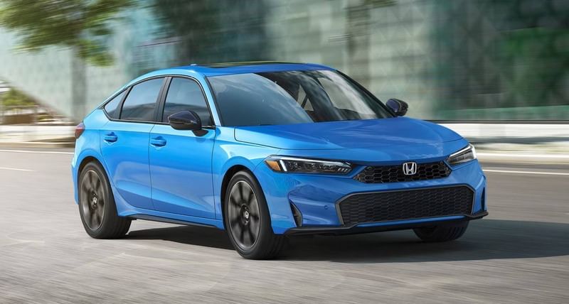 El Honda Civic Hatchback Sport Touring Hybrid 2025 en color Boost Blue Pearl circulando en un entorno urbano