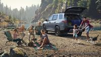 A family having a picnic on the lake shore behind them is a 2023 Honda Pilot TrailSport shown in Sonic Gray Pearl with accessory crossbars. Programmable power tagilgate standard on EX-L and aboce. Power tailgate with hands-free aaccess and Walk Away Close standard on Touring and Elite