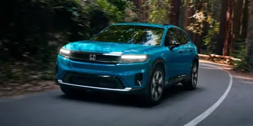 2026 Honda Prologue Elite in North Shore Pearl, driving through redwoods, taking a curved turn on a paved road, with light peeking through the trees in the background.