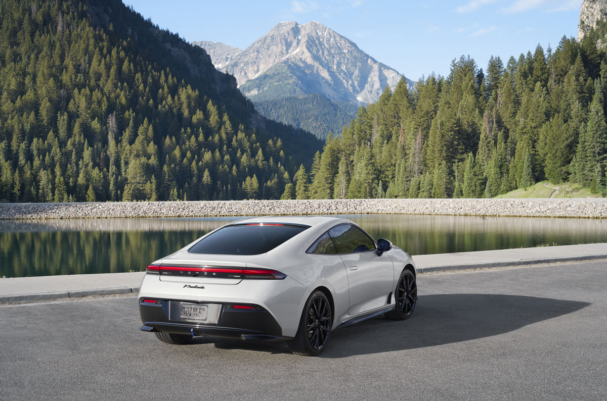 A rear three-quarter view of a silver 2026 Honda Prelude parked next to a calm lake, with a majestic mountain and dense pine forest in the background.