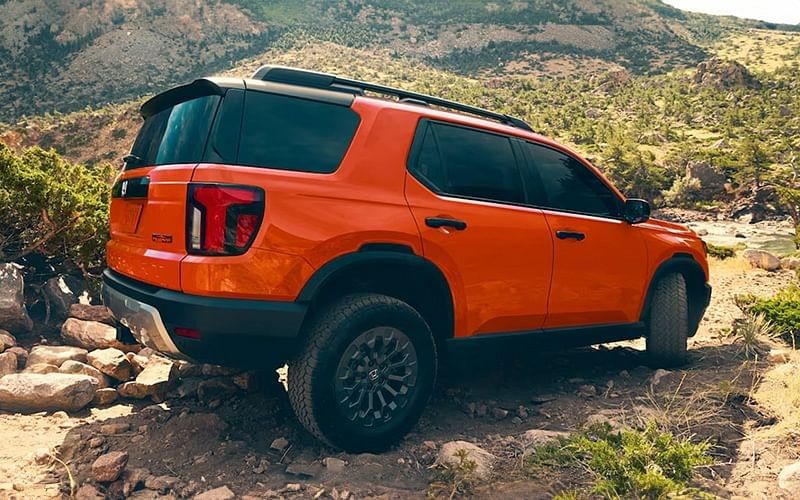 A vibrant orange 2026 Honda Passport featuring a contrasting black roof, displayed in a clear outdoor setting.