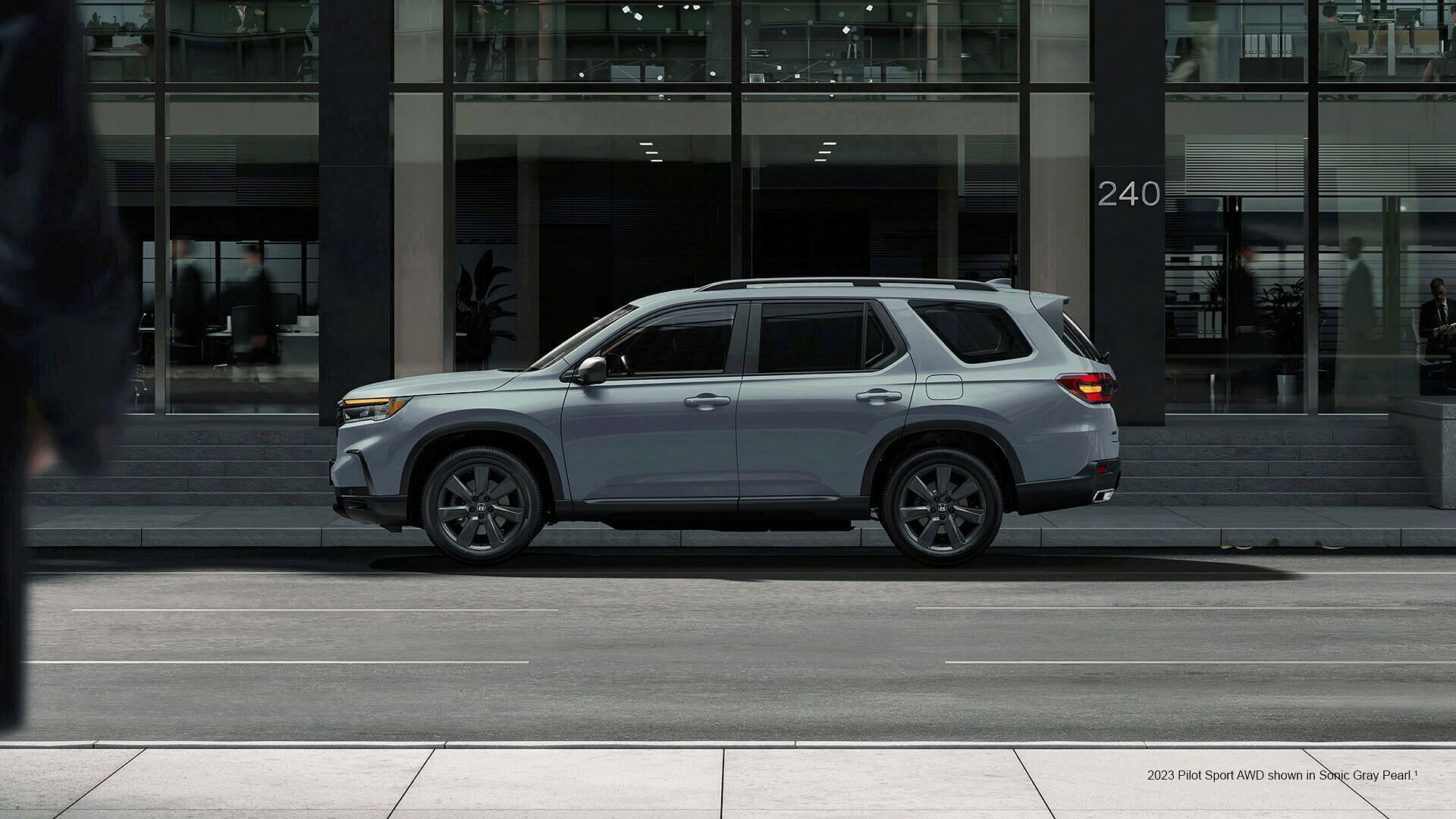 2023 Honda Pilot Sport shown in Sonic Gray Pearl with accessory crossbars standing by the building