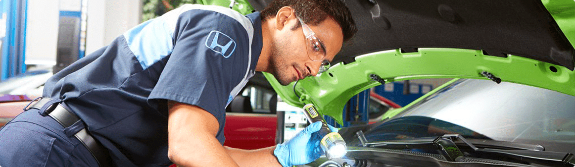 honda service employee checking the condition of the car's engine, holding a flashlight in his left hand