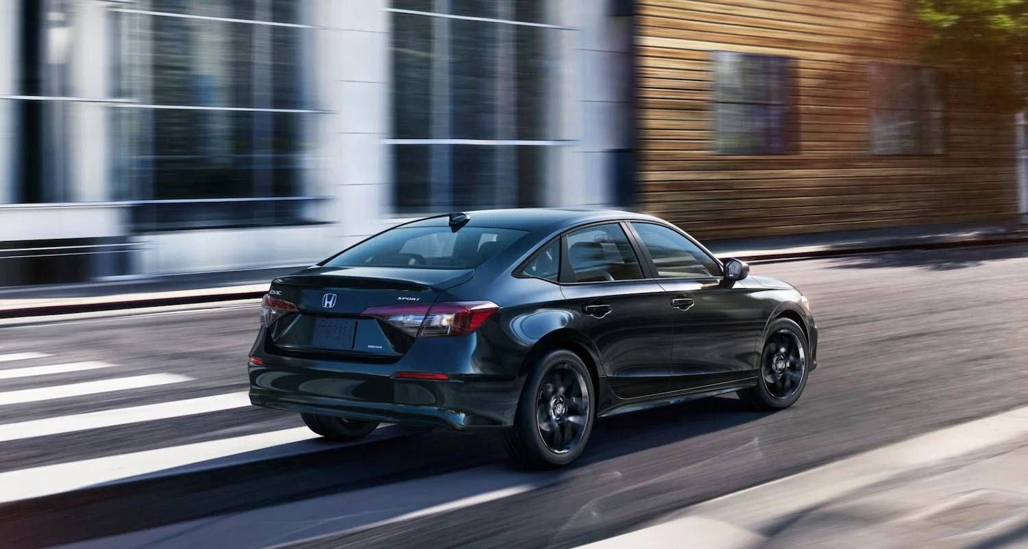 The 2025 Honda Civic Sedan Sport Hybrid in Crystal Black Pearl at 7/8 rear passenger side angle in urban street corner outdoor environment