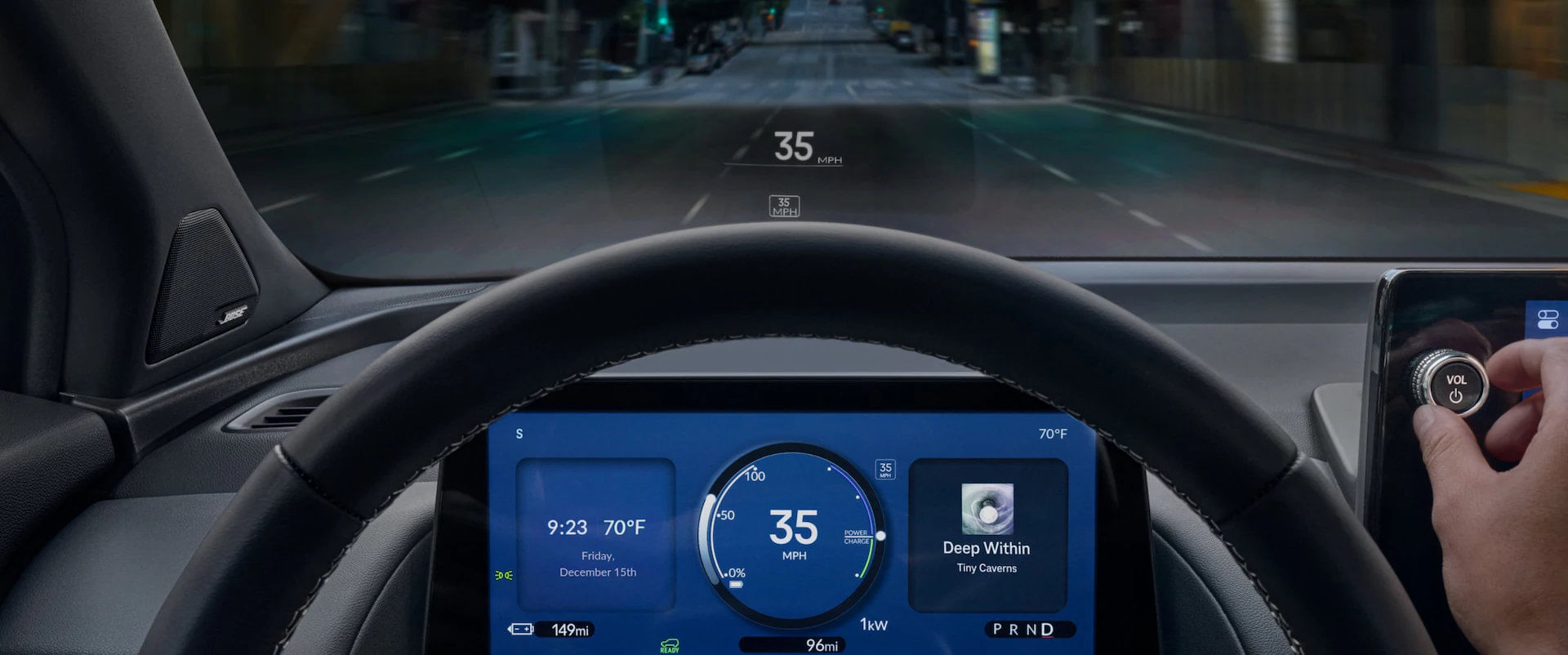 Driver's perspective inside the 2025 Honda Prologue, showing the digital instrument cluster, center infotainment screen, and head-up display projecting speed onto the windshield while driving on a city street at night. A hand adjusts the volume knob.
