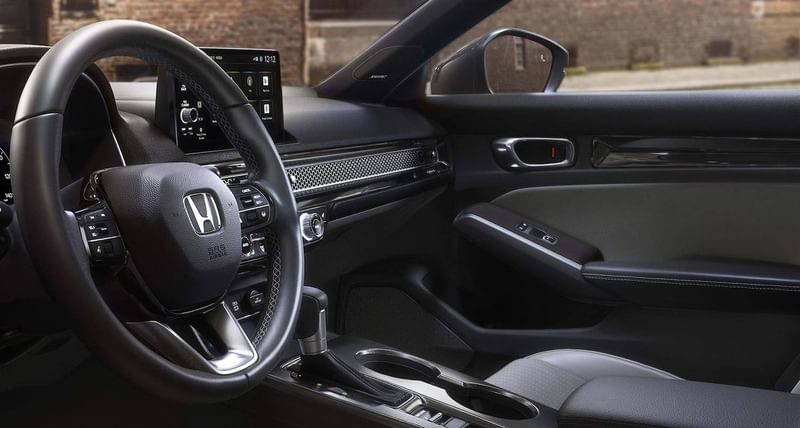 The 2025 Honda Civic Hatchback Sport Touring Hybrid in Meteorite Gray Metallic, front cabin area from driver's door across to passenger view