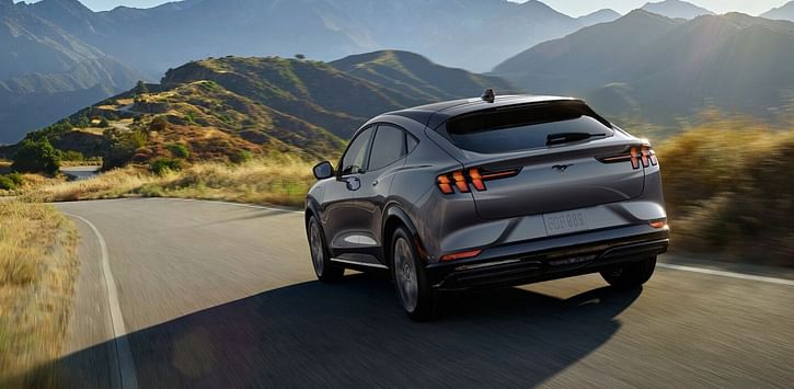 A silver Mustang Mach-E driving down the road in the mountains.