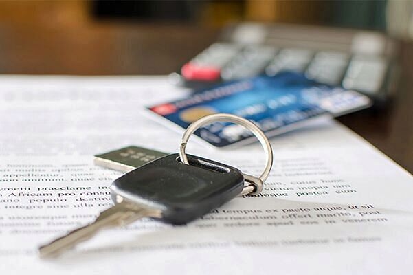 Car keys sitting on a pile of paperwork with a credit card and calculator blurred out in the …