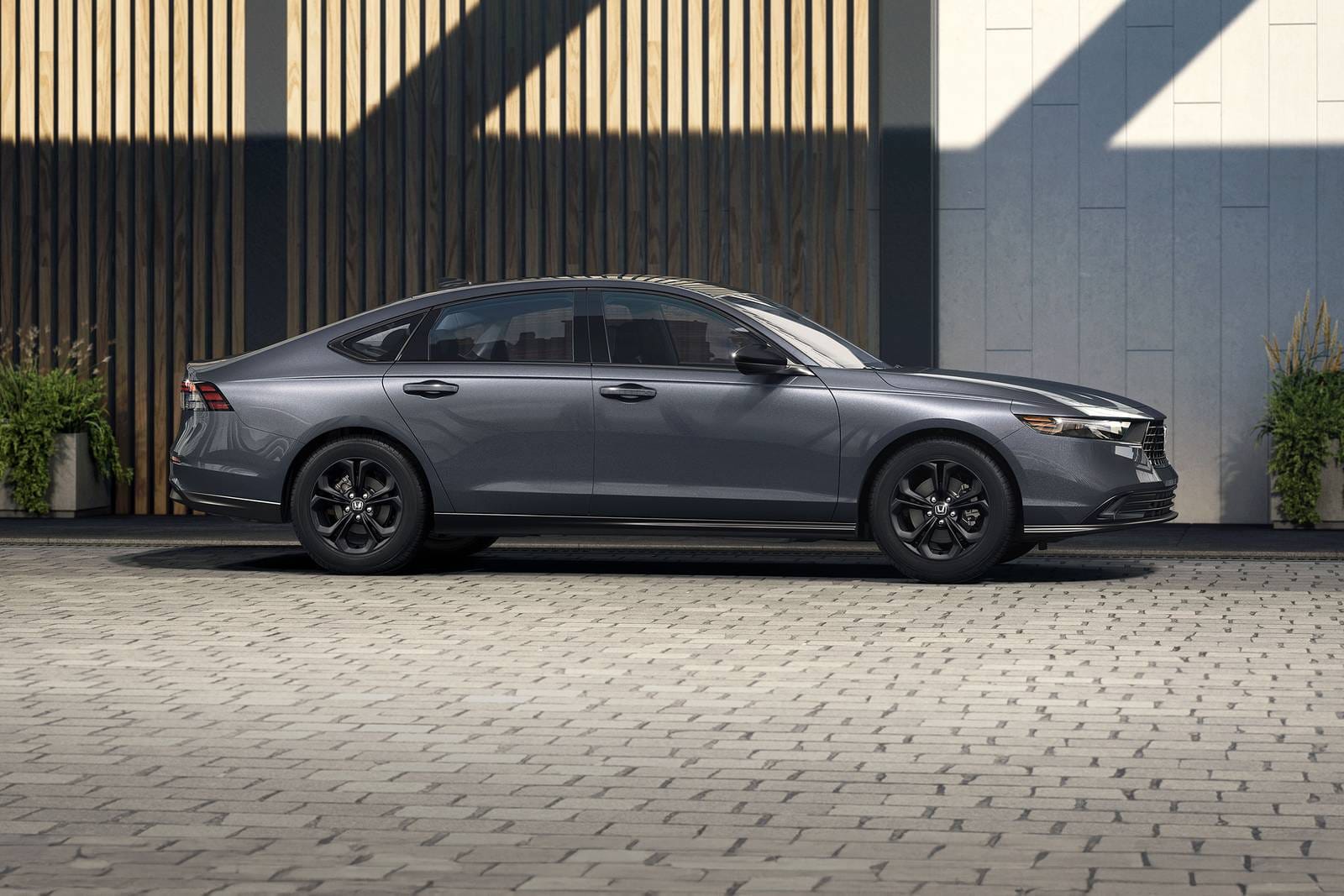 Elegante sedán gris estacionado en un camino de entrada de ladrillos, flanqueado por paredes modernas de madera y piedra con plantas, transmitiendo un sentido de elegancia y sofisticación.