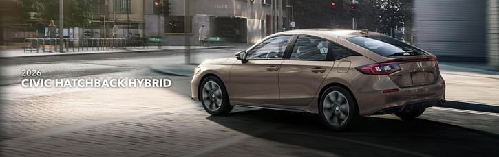 2026 Honda Civic Hatchback Hybrid in motion on an urban street, captured from the rear. Sleek design reflects the afternoon light, conveying modern efficiency.