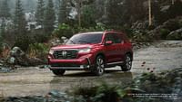 2023 Honda Pilot Elite in Radient Red Metallic II while driving in the rain in the wilderness. Forest in the background