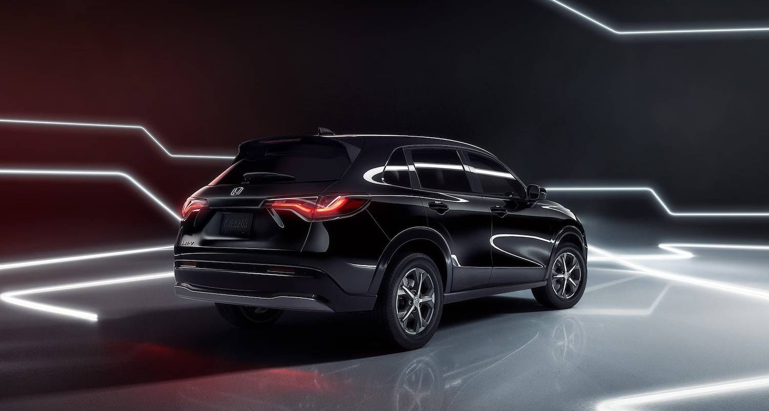 Rear passenger-side view of the 2026 Honda HR-V EX-L in Crystal Black Pearl shown parked on a reflective surface and surrounded by neon lights